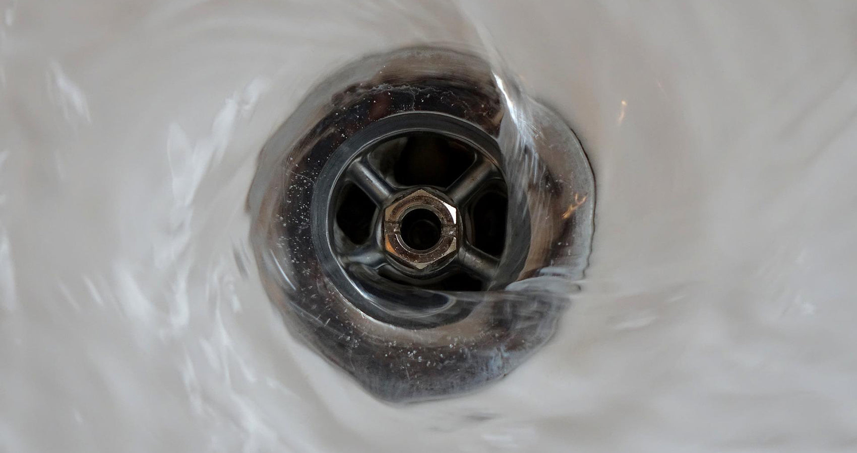 Water swirling down a stainless steel drain in a white basin