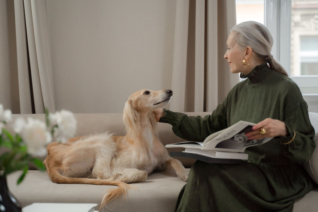 Elegant senior woman reading with a Saluki dog on a living room sofa