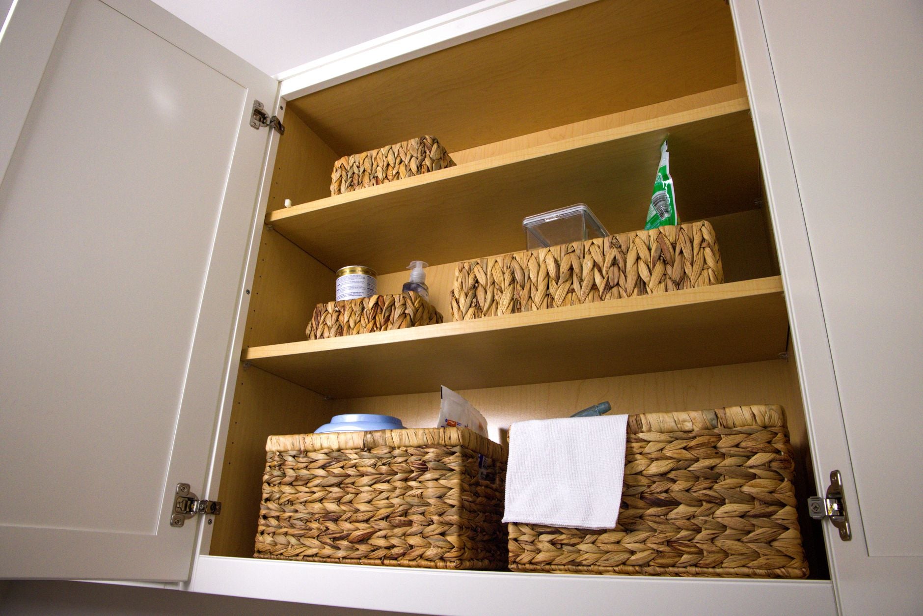 Neat storage in a kitchen cabinet using wicker baskets for a clean aesthetic and organization