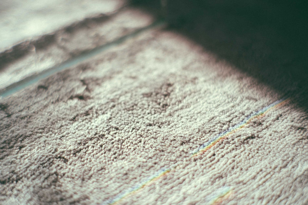 Closeup of gray textured carpet with thin colorful lines placed on floor in room with bright sunlight and shadow at home